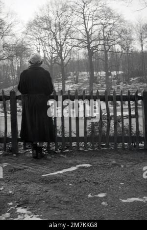 1950s, historique, vue de l'arrière, une jeune femme portant un long manteau en velours côtelé, un petit chapeau, des gants et des bottines qui se tiennent au-dessus d'un lac gelé dans les bois, Farningham, Kent, Angleterre, Royaume-Uni. Banque D'Images