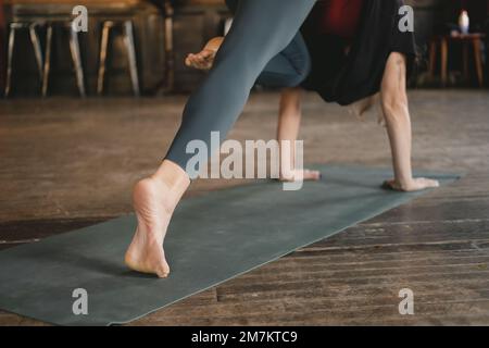 Femme non reconnaissable yogi nouveau professeur faisant un chien à trois pattes face vers le bas pose genou à nez, entraînement de yoga, pieds nus et portant des sportswe Banque D'Images