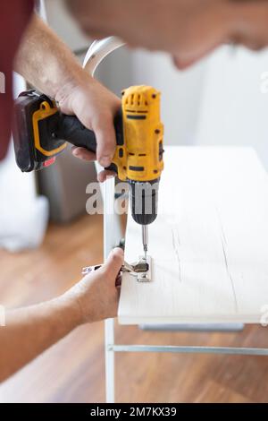 Gros plan de l'homme assemblant des meubles à l'aide d'un tournevis sans fil Banque D'Images