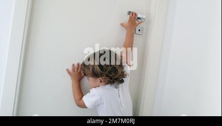 Bébé essayant d'atteindre le bouton de la porte. Enfant sur les orteils de pointe atteignant pour la porte Banque D'Images