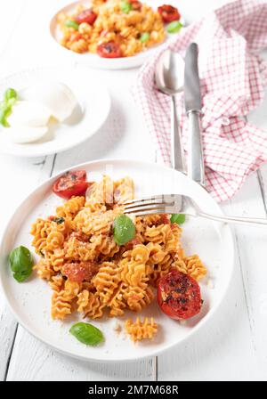 Pâtes avec sauce tomate mozzarella, parmesan et tomates cerises rôties sur une assiette sur fond blanc Banque D'Images