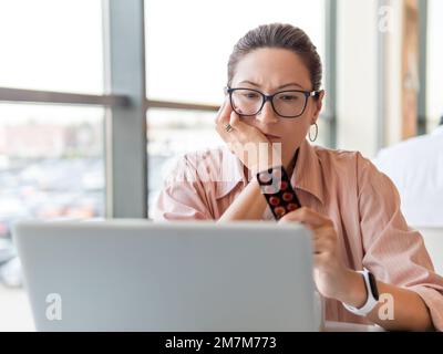 Une femme qui frognait regarde des pilules de médicaments tout en travaillant avec un ordinateur portable. Problèmes de santé mentale, épuisement émotionnel ou maux de tête. Bureau moderne Banque D'Images