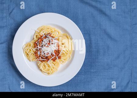 Spaghetti à la bolognaise avec parmesan sur une assiette blanche. Décor et arrière-plan bleus simples. Plats italiens traditionnels, cuisine méditerranéenne Banque D'Images