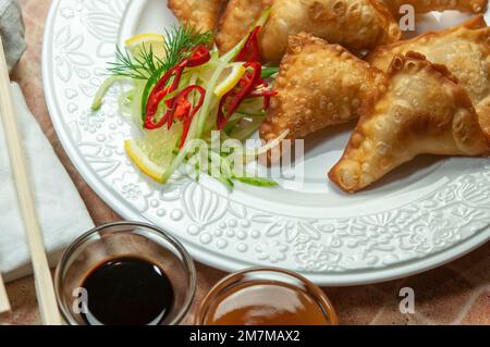 Boulettes frites asiatiques wontons au soja et sauce aigre-douce sur un plat blanc. Boulettes frite gyoza avec sauce soja, et baguettes, foyer sélectif. Banque D'Images