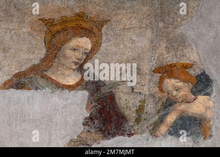 Belle Madonna couronnée aux yeux bleus avec de longs cheveux dorés ou auburn regarde le Christ enfant en haled : Fresque Renaissance restaurée mais fragmentaire, peinte en 1512, sur le front ouest de l'ancienne Cappella di San Grato (Chapelle de St Gratus) dans la via Jean-Baptiste de Tillier à Aoste, capitale régionale de la Valle d'Aoste, dans le nord-ouest de l'Italie. Banque D'Images