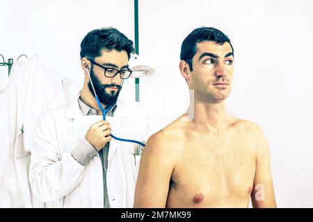 Jeune hipster médecin primaire au travail ausculting homme patient dans la clinique privée - concept de médecine alternative moderne dans blanc propre prof médical Banque D'Images