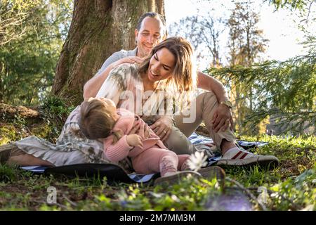 Europe, Allemagne, Bade-Wurtemberg, Stuttgart, Château de Hohenheim, Bonne famille assise sur une couverture de pique-nique sous l'arbre Banque D'Images