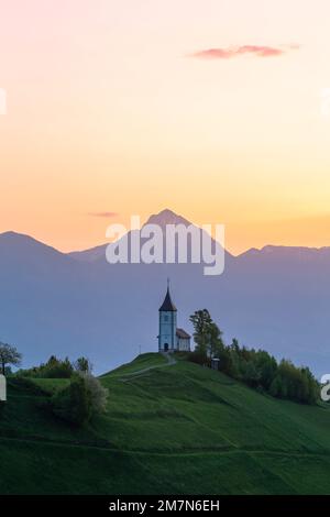 L'église emblématique de Jamik, avec le Mont Triglav en arrière-plan au lever du soleil. Jamnik, Kranj, haute-Carniola, Slovénie. Banque D'Images