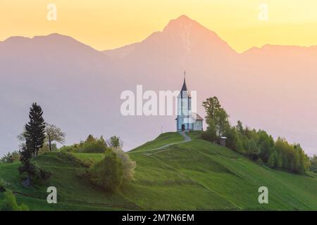L'église emblématique de Jamik, avec le Mont Triglav en arrière-plan au lever du soleil. Jamnik, Kranj, haute-Carniola, Slovénie. Banque D'Images