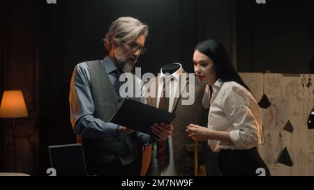 Les tailleurs hommes et femmes travaillent sur un costume d'affaires ou de mariage. L'homme dessine un croquis sur une tablette. Mannequin en costume tailleur dans un atelier de designer ou de tailleur. Mode et artisanat. Banque D'Images