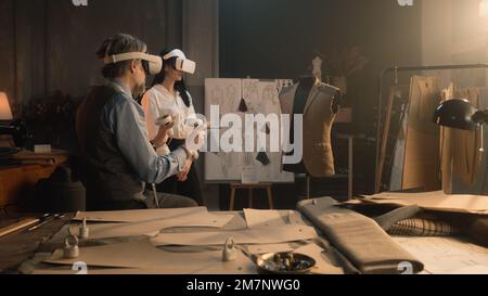 Les tailleurs portant un casque VR avec des contrôleurs sans fil. Ils travaillent dans un atelier de luxe ou de personnalisation et créent des combinaisons de désherbage en réalité virtuelle. Concept de technologies de l'avenir dans les affaires. Banque D'Images
