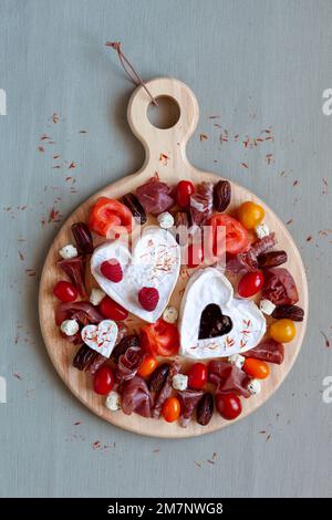 Plateau de fromages de la Saint-Valentin avec fromage en forme de coeur, charcuterie, tomates et fruits, vue de dessus Banque D'Images