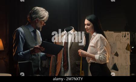 Les tailleurs hommes et femmes travaillent sur un costume d'affaires ou de mariage. L'homme dessine un croquis sur une tablette. Mannequin en costume tailleur dans un atelier de designer ou de tailleur. Mode et artisanat. Banque D'Images