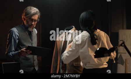 Les tailleurs hommes et femmes travaillent sur un costume d'affaires ou de mariage. L'homme dessine un croquis sur une tablette. Mannequin en costume tailleur dans un atelier de designer ou de tailleur. Mode et artisanat. Banque D'Images