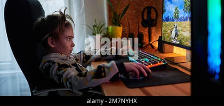 Image de l'immergé teenage boy joueur à jouer à des jeux vidéo sur ordinateur dans la pièce sombre portant des écouteurs et à l'aide clavier coloré rétroéclairé Banque D'Images