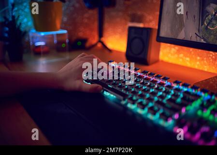 Gros plan des mains montrant un joueur en appuyant sur les boutons du clavier tout en jouant à un jeu vidéo en ligne. Voyants du clavier. La chambre est sombre. Banque D'Images