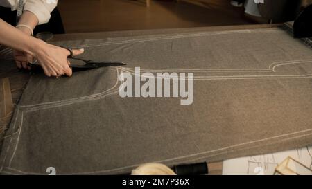 Une femme professionnelle coupe le tissu selon le croquis à l'aide de ciseaux pour la couture. Processus de fabrication de vêtements dans un atelier de designer de luxe ou un atelier de couture. Mode et artisanat. Banque D'Images