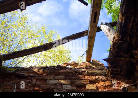 Ancienne maison en ruines abandonnée. Mur de briques pelées, restes de bois du toit. Par le trou dans le toit vous pouvez voir le ciel bleu vif et le gr Banque D'Images