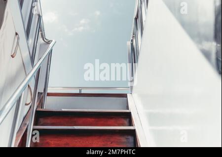 Un cliché capturé du pont inférieur lors de l'escalade d'un escalier en bois et de rampes métalliques brillantes menant au pont supérieur d'un voilier blanc ; on Banque D'Images