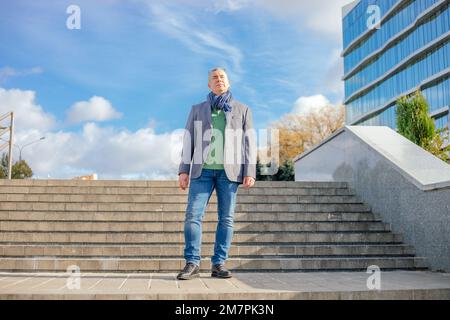 Vieux homme d'affaires en foulard élégant se tiennent sur des escaliers pavés sur fond bleu ciel, de la vue d'en dessous. Homme marche à l'extérieur. Banque D'Images