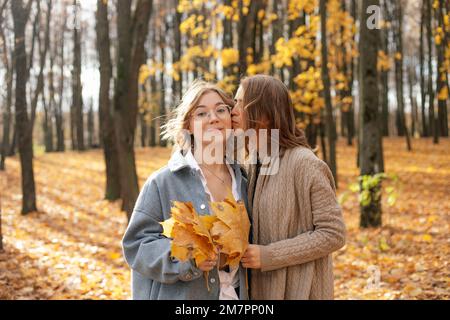 Mère baiser dans joue fille adolescente dans la forêt ensoleillée. Les filles tiennent des feuilles d'érable jaune tombées et marchent dans le parc d'automne. Banque D'Images