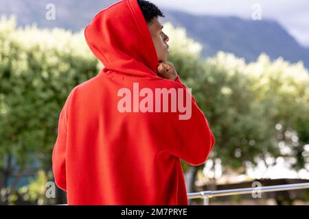 Image de l'homme biracial dans le haut à capuchon rouge avec l'espace d'imitation sur les arbres en arrière-plan Banque D'Images