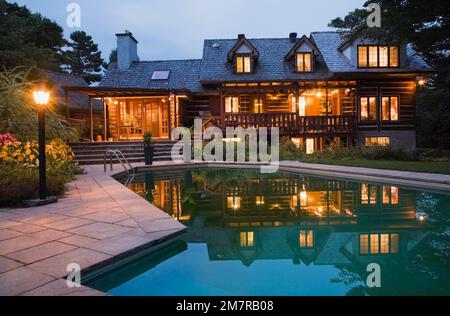 Piscine creusée et arrière de maison en rondins de style cottage reconstruite de 1976 au crépuscule. Banque D'Images