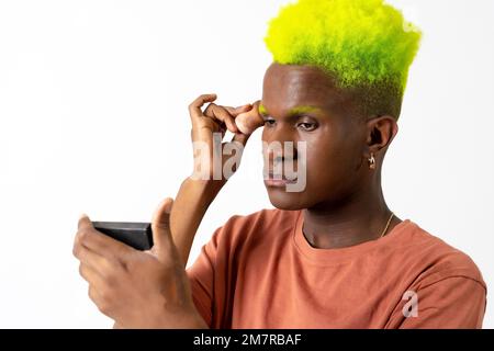 Un homme noir androgyne posant sur le maquillage, concept LGTBI, appliquant le blush avec un miroir Banque D'Images