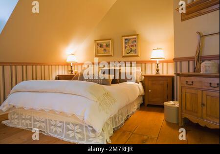 Lit queen size dans la chambre principale avec lambris à l'étage à l'intérieur de la vieille maison en rondins de style cottage reconstruite des années 1850. Banque D'Images