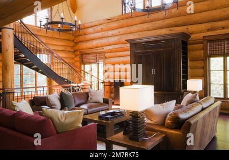 Canapés en cuir marron et Bordeaux et table basse en bois dans le salon avec lustres de style médiéval à l'intérieur de la luxueuse maison en rondins de style scandinave. Banque D'Images