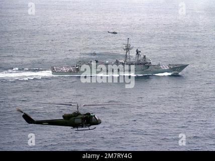 Vue aérienne à tribord du frégate australien HMAS CANBERRA (F-02) lors de son premier lancement de missile Harpoon près du Pacific missile Test Center, point Mugu, Californie. Deux hélicoptères UH-1 Iroquois assurent la couverture aérienne du lancement. Pays : Océan Pacifique (POC) Banque D'Images