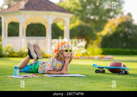 Devoirs de jeu et dessin d'art artisanal pour enfants. Un garçon d'école intelligent qui fait ses devoirs, écrit sur un livre de copie dans l'herbe verte du parc. Retour à l'école, la connaissance Banque D'Images