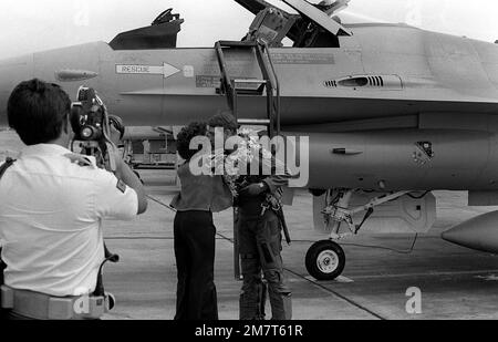 A son arrivée à Hawaï, le pilote de cet avion Faucon de combat F-16A de l'Armée de l'Air qui vient d'atterrir reçoit l'anneau traditionnel de fleurs autour de son cou et un baiser d'une jolie dame. Le F-16A est issu de l'escadron de combat tactique 428th situé à la base aérienne de Nellis, Nevada, et il est ici pour voler avec des avions fantômes F-4 marins à l'appui des unités de l'Armée de terre basées à Hawaï. L'événement est un exercice des chefs d'ÉTAT-MAJOR interarmées, qui durera un mois (du 2 octobre au 2 novembre 1981). Base: Marine corps Air Station Kaneohe État: Hawaii (HI) pays: Etats-Unis d'Amérique (USA) Banque D'Images