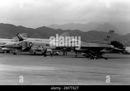 Un avion Faucon de combat F-16A de la Force aérienne est dirigé par un homme d'équipage au sol et est stationné à côté de deux avions F-4 Phantom II marins. Le F-16A est issu de l'escadron tactique de combat 428th situé à la base aérienne de Nellis, au Nevada, et il est ici pour voler avec des avions F-4 Phantom II marins à l'appui des unités de l'Armée de terre basées à Hawaï. L'événement est un exercice des chefs d'ÉTAT-MAJOR interarmées, qui durera un mois (du 2 octobre au 2 novembre 1981). Base: Marine corps Air Station Kaneohe État: Hawaii (HI) pays: Etats-Unis d'Amérique (USA) Banque D'Images