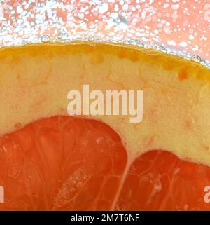 Vue rapprochée de la tranche de pamplemousse rouge sur fond d'eau. Texture de la boisson fraîche aux fruits avec macro bulles sur la paroi en verre. Conception plate. Banque D'Images