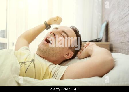 Jeune homme s'étirant tout en se réveillant le matin. Un homme qui bâille tout en se réveillant. Jeune homme paresseux en sommeil. Portrait de l'homme bâille et s'étire dans le lit. Banque D'Images