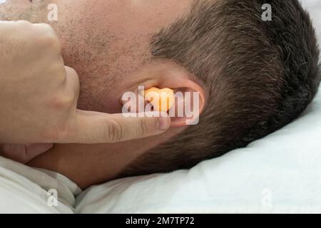 beau jeune homme dormant, dans les oreilles boules d'oreille orange contre le bruit de la rue, salut de voisins bruyants. quand empêcher le sommeil. une prise dans les oreilles pour Banque D'Images