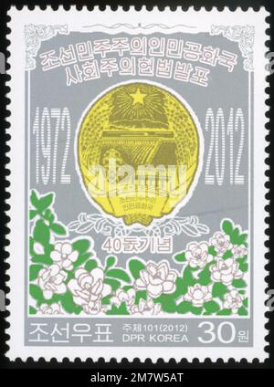 Timbre-poste nord-coréen de 2012 commémorant le 40ème anniversaire de la Constitution socialiste, représentant l'emblème national et le magnolia. Banque D'Images