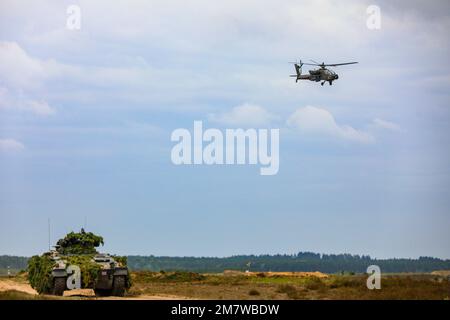 A ÉTATS-UNIS Armée AH-64E gardien d'Apache affecté au Palehorse de la Force opérationnelle de l'escadron 7th, 17th Cavalry Regiment, 1st Air Cavalry Brigade, vole au-dessus d'un transporteur de personnel blindé allemand pendant un exercice d'entraînement multinational sur le terrain durant Defender Europe 2022, Drawsko Pomorskie, Pologne, 15 mai 2022. Defender Europe 22 est une série d'États-Unis L'armée européenne et l'Afrique exercices de formation multinationaux en Europe de l'est. L'exercice démontre les États-Unis La capacité de l’armée européenne et de l’Afrique à mener des opérations de combat au sol à grande échelle sur plusieurs théâtres soutenant l’OTAN. Banque D'Images