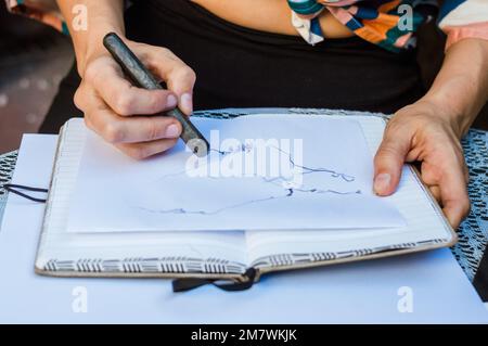 gros plan d'une femme caucasienne inreconnaissable assise à l'extérieur, dessin sur un papier sur un carnet avec graphite, concept art, espace de copie. Banque D'Images