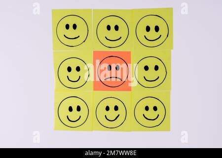 triste couleur orange visage surrouillé par heureux jaune smiley personnes dessinées comme graphiques sur tramsparentes notes adhésives isolées sur un fond blanc Banque D'Images