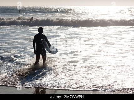 Les surfeurs se promène le long de la plage après un moment amusant dans l'eau. L'image est rétro-éclairée et présente le sujet en silhouette. Banque D'Images
