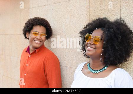 Couple ethnique élégant regardant latéralement contre un mur de briques. Banque D'Images