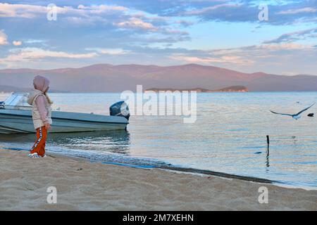 Kurbulik, République de Buryatia, Russie - 11 juillet 2022 : une fille nourrit des mouettes sur le lac Baikal dans la baie de Chivyrkuy pendant le coucher du soleil Banque D'Images