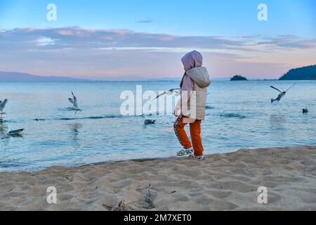 Kurbulik, République de Buryatia, Russie - 11 juillet 2022 : une fille nourrit des mouettes sur le lac Baikal dans la baie de Chivyrkuy pendant le coucher du soleil Banque D'Images