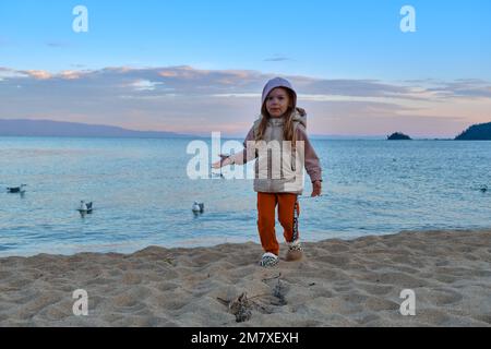 Kurbulik, République de Buryatia, Russie - 11 juillet 2022 : une fille nourrit des mouettes sur le lac Baikal dans la baie de Chivyrkuy pendant le coucher du soleil Banque D'Images