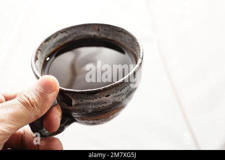 Main d'un homme tenant une tasse de café chaud noir sur fond blanc Banque D'Images