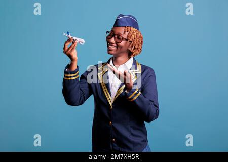 Un agent de bord afro-américain en uniforme de travail tenant un avion modèle. Hôtesse montrant un avion à l'échelle commerciale avec un espace pour la publicité aérienne en studio. Banque D'Images