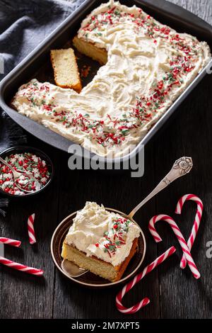 gâteau de noël en feuille de vanille avec glaçage à la crème fouettée garni de saupoudrés dans un plat de cuisson avec tranche sur une pelle à gâteau sur une table en bois sombre, Banque D'Images