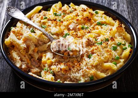 Thon Mornay, crémeux Thona Casserole Penne Pasta Bake dans un plat de cuisson sur une table en bois sombre avec une cuillère, gros plan Banque D'Images